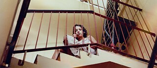 Persona sentada en un descanso de escalera interior detrás de una baranda metálica.
