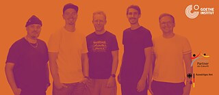Bandfoto der Munich Supercrew zur Südafrika-Tour 2026 mit fünf Bandmitgliedern vor orangefarbenem Hintergrund.