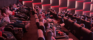 In einem Kinosaal stricken die Zuschauer*innen bei gedimmtem Licht während der Filmvorführung