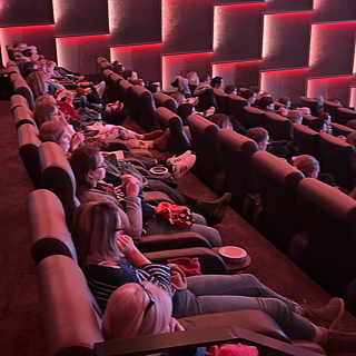 In einem Kinosaal stricken die Zuschauer*innen bei gedimmtem Licht während der Filmvorführung