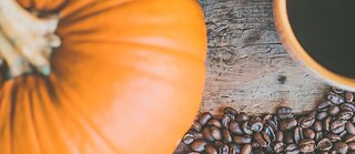 Rustikale Herbstszene mit Kaffeebohnen, Kürbis und Kaffeetasse auf einem Holztisch