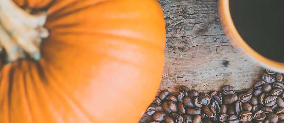 Rustikale Herbstszene mit Kaffeebohnen, Kürbis und Kaffeetasse auf einem Holztisch