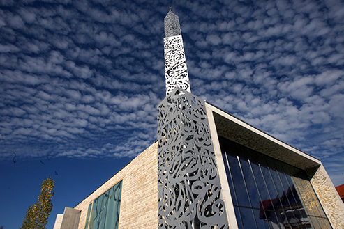 The prayer room of the Penzberg Mosque is bathed in azure light streaming in through the dark blue, shimmering facade made of thousands of shards of glass. 