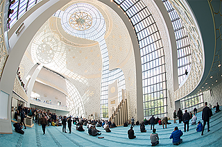 Der Neubau der Zentralmoschee in Köln zeigt: Die Architektur für Moscheen ist den Hinterhöfen entwachsen. Im Innenraum bilden 1.800 Stuckplatten an den Wänden geometrische Muster. Ein gewaltiger Kronleuchter setzt arabische Kalligrafien in Szene.
