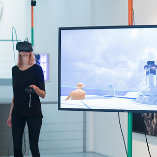 Eine Frau mit einer VR-Brille steht vor einem großen Bildschirm.