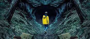 Un joven con un impermeable amarillo a la entrada de una cueva en el bosque