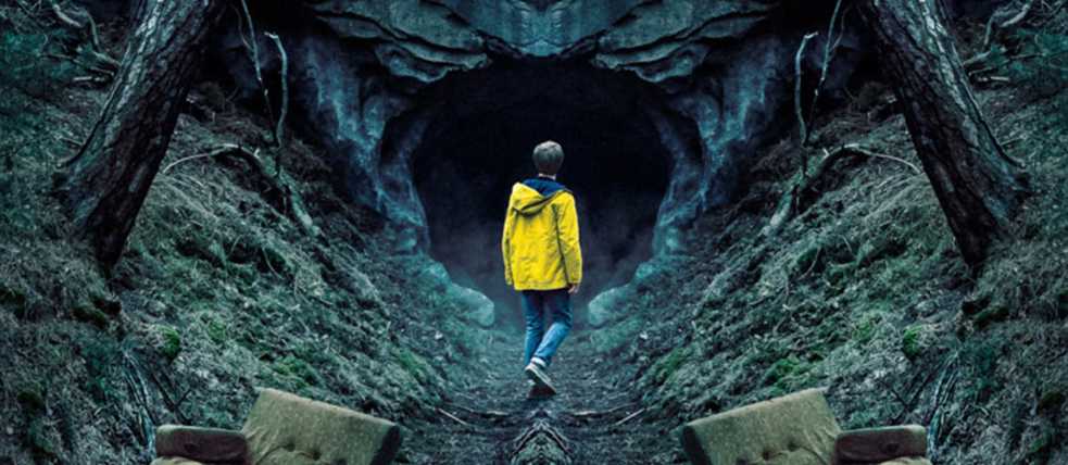 Un joven con un impermeable amarillo a la entrada de una cueva en el bosque