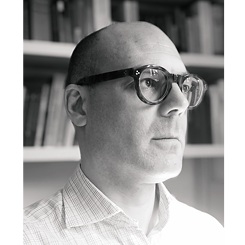 Portrait image of Michael Zichy in grayscale; he is wearing glasses and a checkered shirt