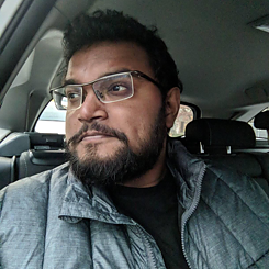 Portrait of Yudhanjaya Wijeratne; he is sitting in a car and wears short hair and glasses