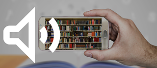 A hand holds a smartphone, on its screen a bookshelf can be seen